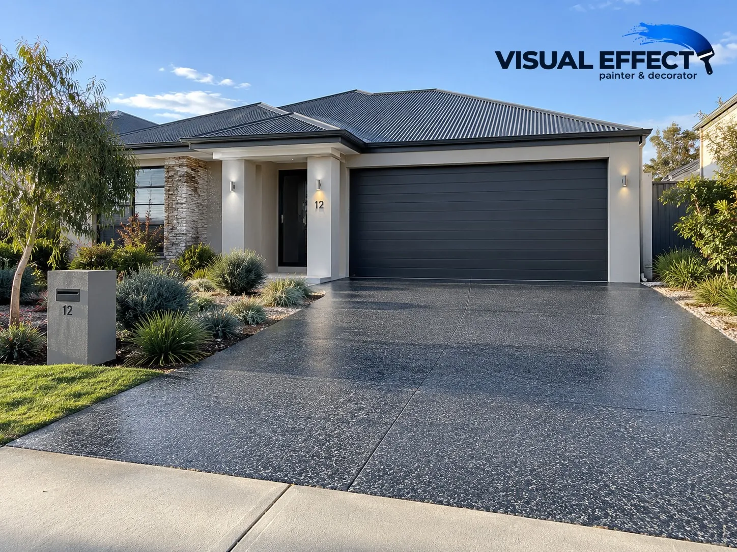 Freshly sealed charcoal exposed-aggregate driveway in front of a rendered home